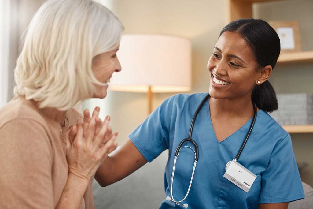 Older resident speaking with an interviewer in a bright assisted living common room with a notebook nearby